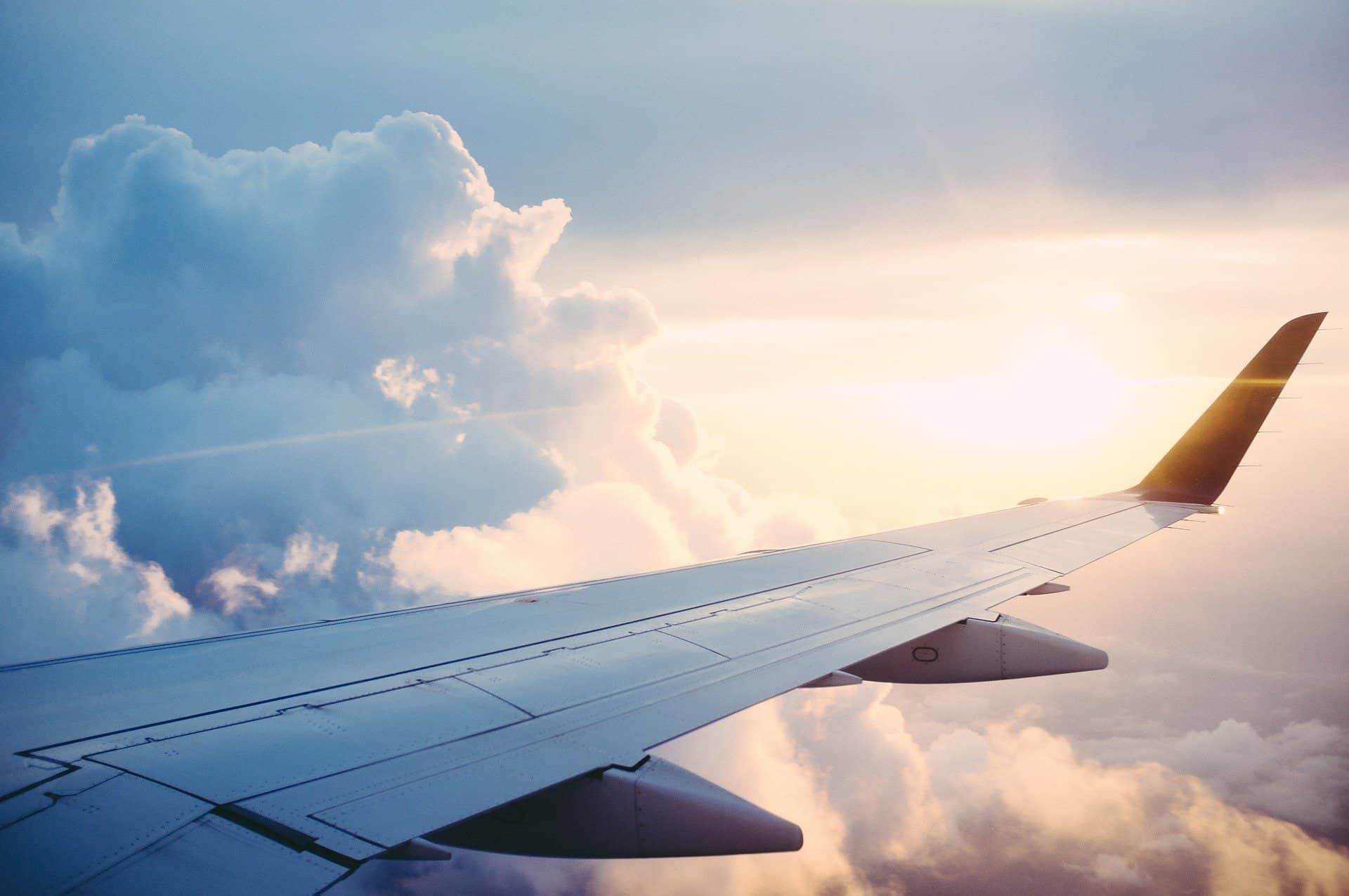 Aerial view of an airplane wing flying through the sky with clouds and sunlight, showcasing travel, aviation, and sky travel experiences.