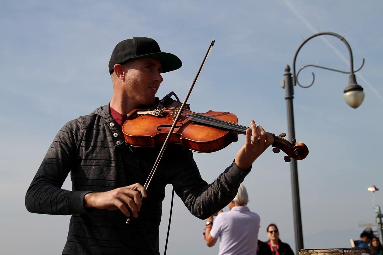 Viral violinist performing outdoors during daytime, street music scene, casual urban environment, talented musician playing classical instrument, live street entertainment, community gathering, public space, outdoor music performance.
