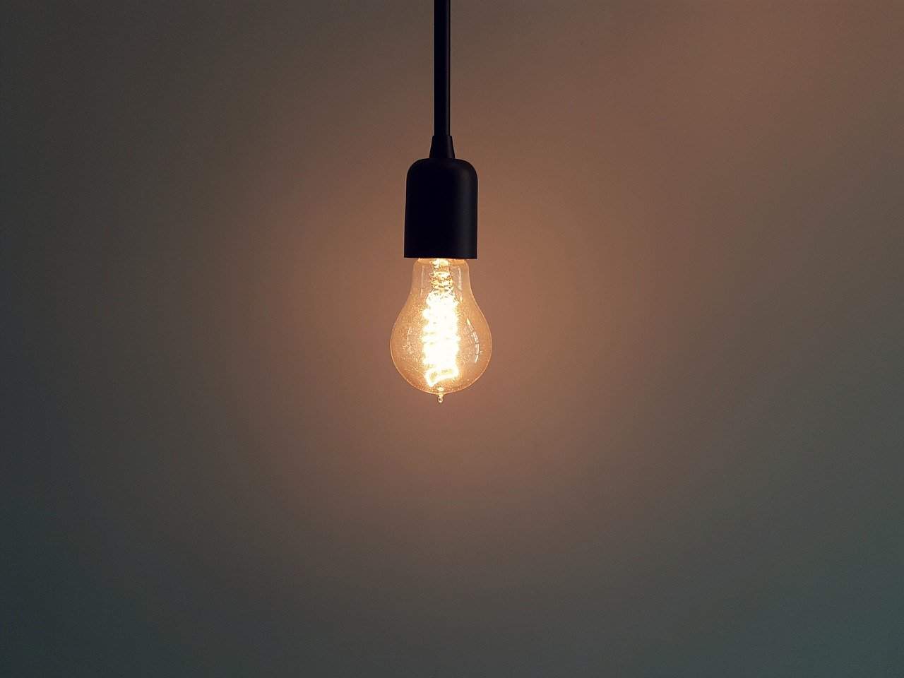Illuminated vintage incandescent light bulb hanging against a plain wall, symbolizing lighting design, energy, or creativity.