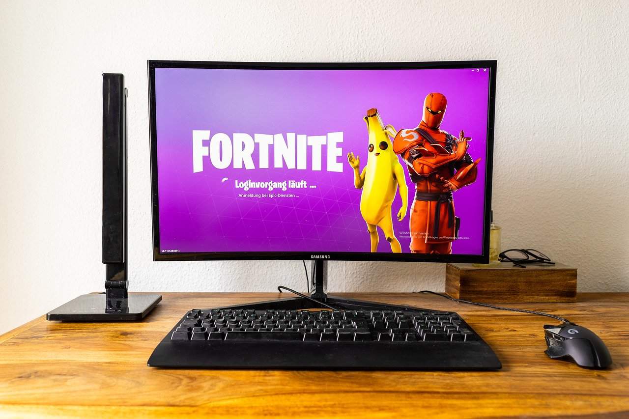 Computer monitor displaying Fortnite login screen with characters on a wooden desk, gaming setup, and related digital entertainment technology.