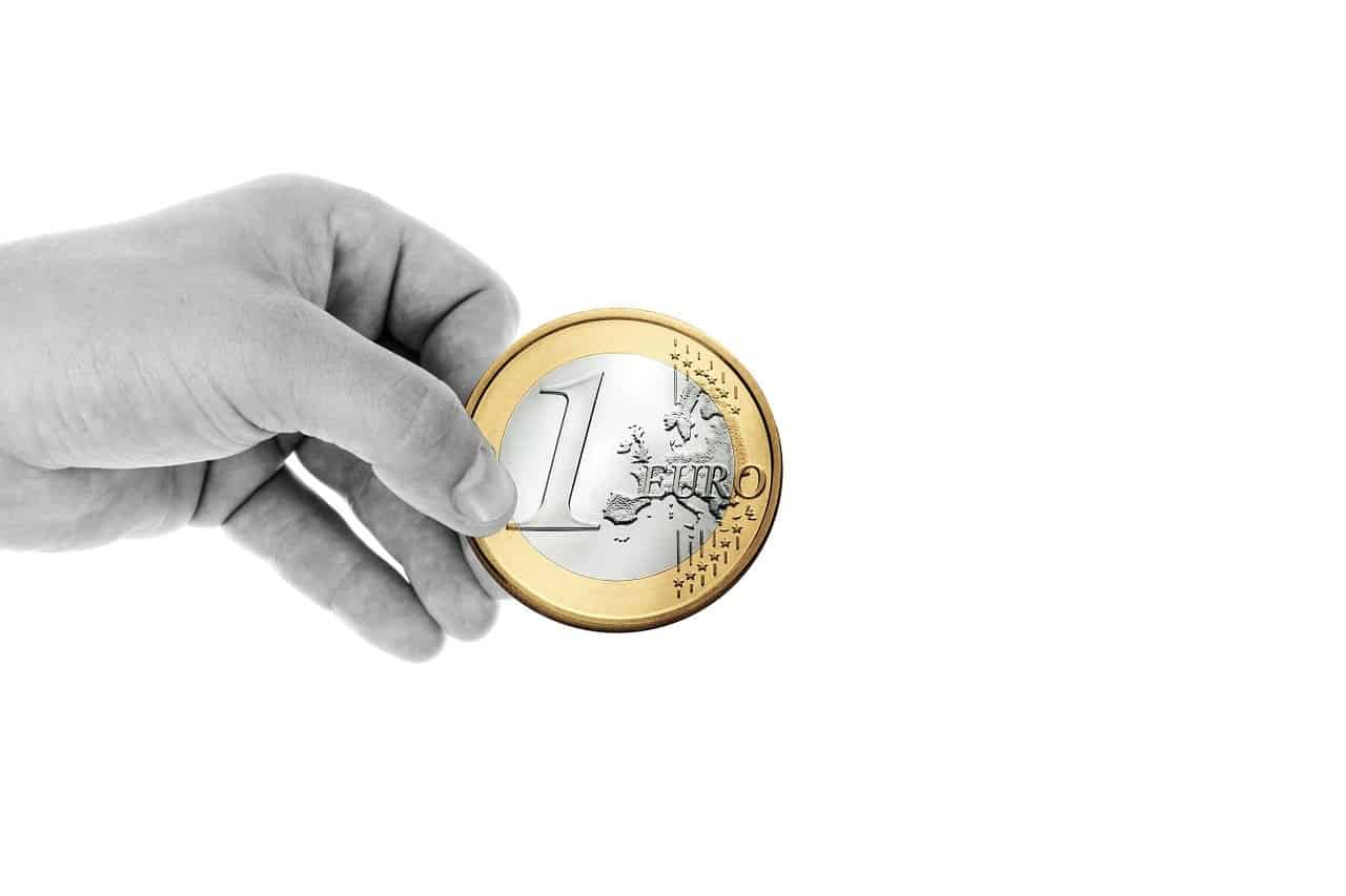 Euro coin held between thumb and forefinger on a white background, symbolic of currency and financial concepts.