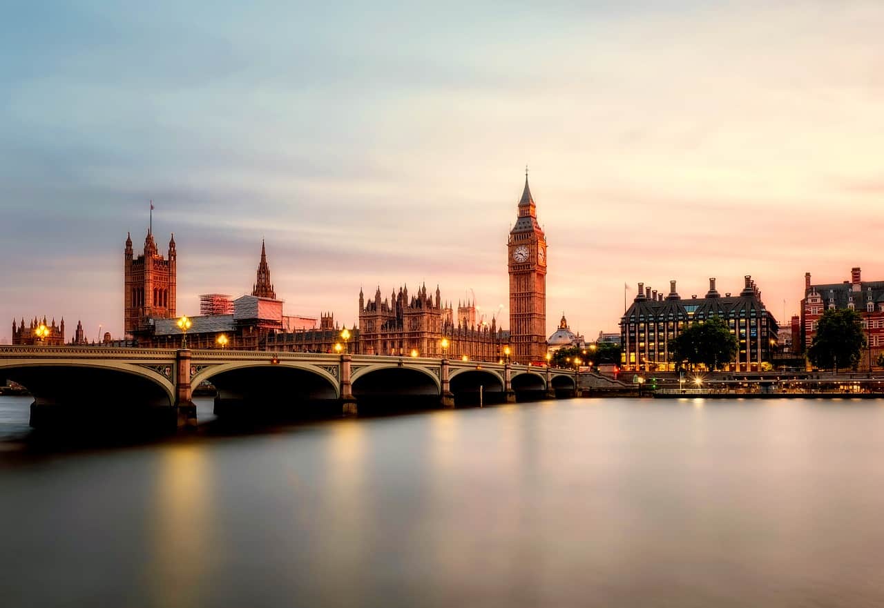 London skyline with Big Ben and Houses of Parliament at sunset, featuring the Westminster Bridge over the River Thames. Iconic UK landmarks illuminated during twilight, showcasing the historic architecture of London.