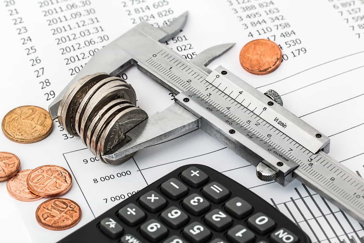 Coins and a calculator on financial documents with a caliper measuring coins, symbolizing financial analysis and cost measurement.