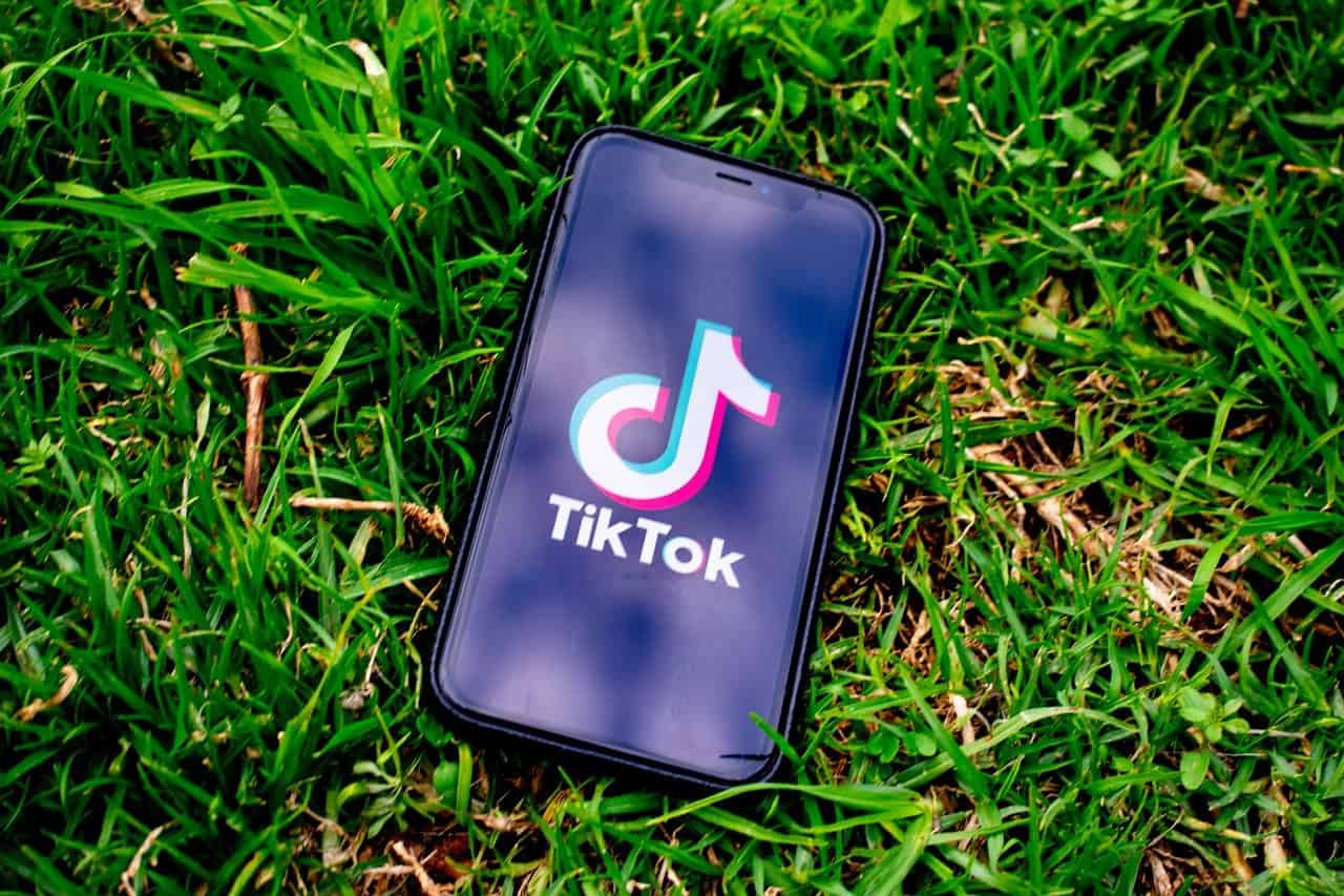 TikTok app on smartphone in lush green grass for social media, short-form video platform, digital entertainment, viral videos, mobile technology, trending content, influencer marketing, social media marketing, app promotion.
