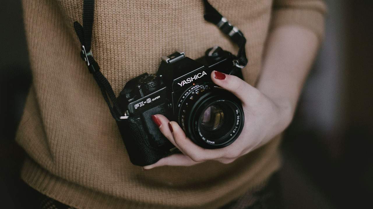 Vintage Yashica film camera held by a person with painted nails, showcasing classic photography gear.