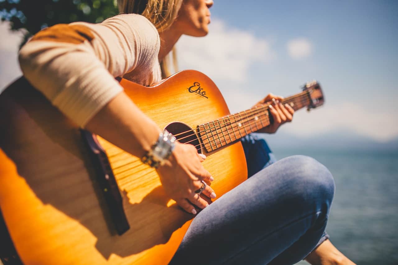 Guitarist playing acoustic guitar outdoors with scenic ocean view, showcasing music, live performance, and outdoor musical expression.