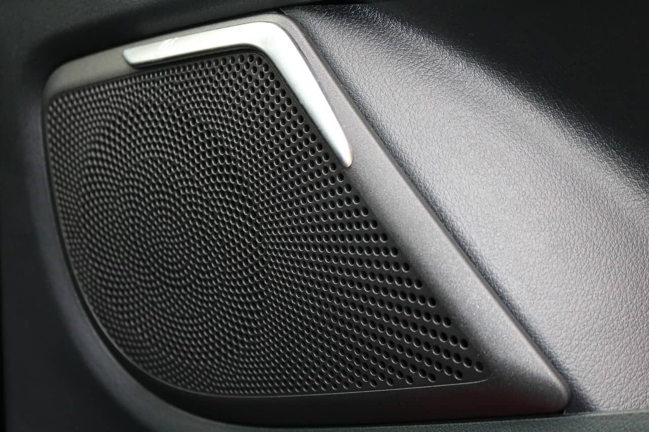 High-quality car speaker grille mounted on vehicle door panel, close-up view showing detailed perforated metal design for premium sound experience, automotive audio system component.