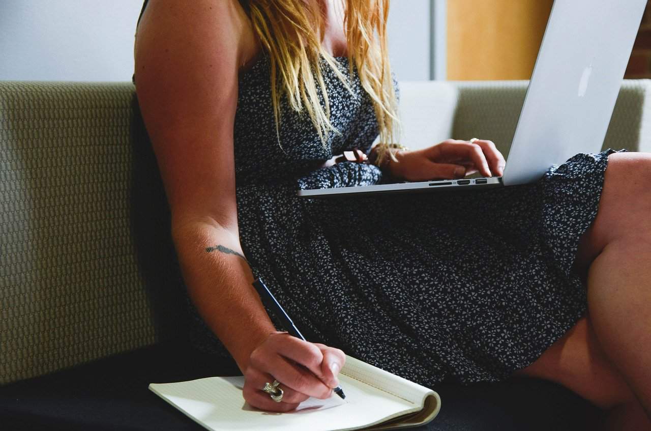 Woman using laptop and writing in notebook, modern workspace, digital content creation, remote work, freelancing lifestyle, Hypebot, music industry news, technology, social media, digital marketing, online business.