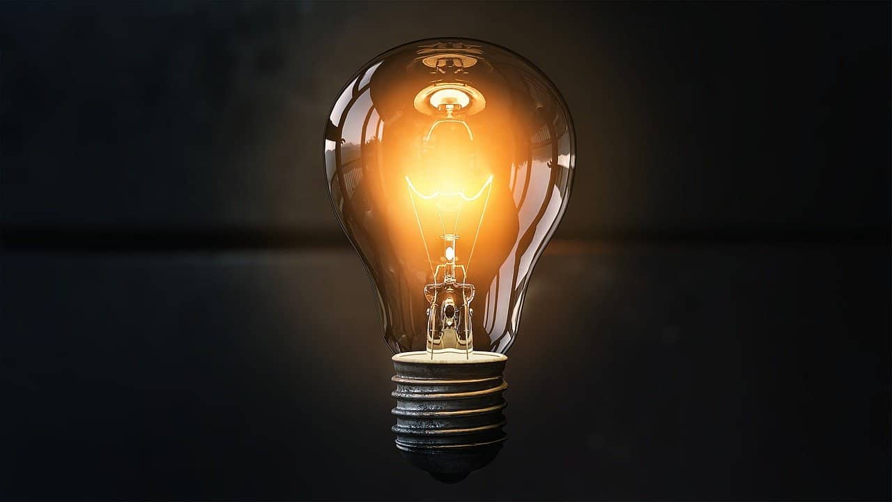 Illuminated incandescent light bulb glowing with warm filament in dark background.