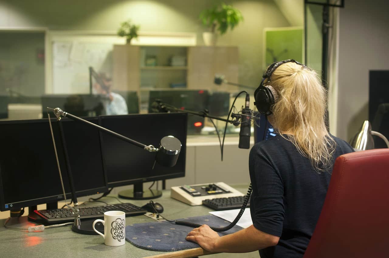 Recording studio with a woman in headphones speaking into a microphone, surrounded by professional audio equipment, showcasing music production and podcast recording environment.