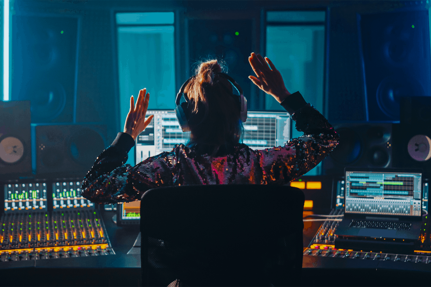 Music producer working at digital audio workstation in recording studio with mixing consoles and speakers, high-tech music production environment, vibrant blue lighting, Hypebot, music industry news and insights.