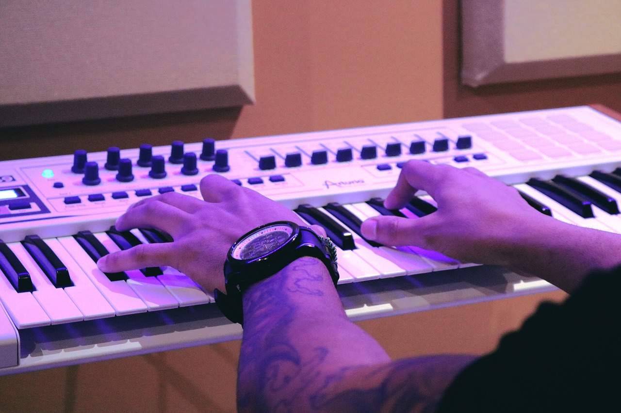 Keyboard synthesizer performance with musician hands, LED lights, and sound control knobs, capturing music production, live music, digital music gear, and electronic keyboard technology for music industry insights.