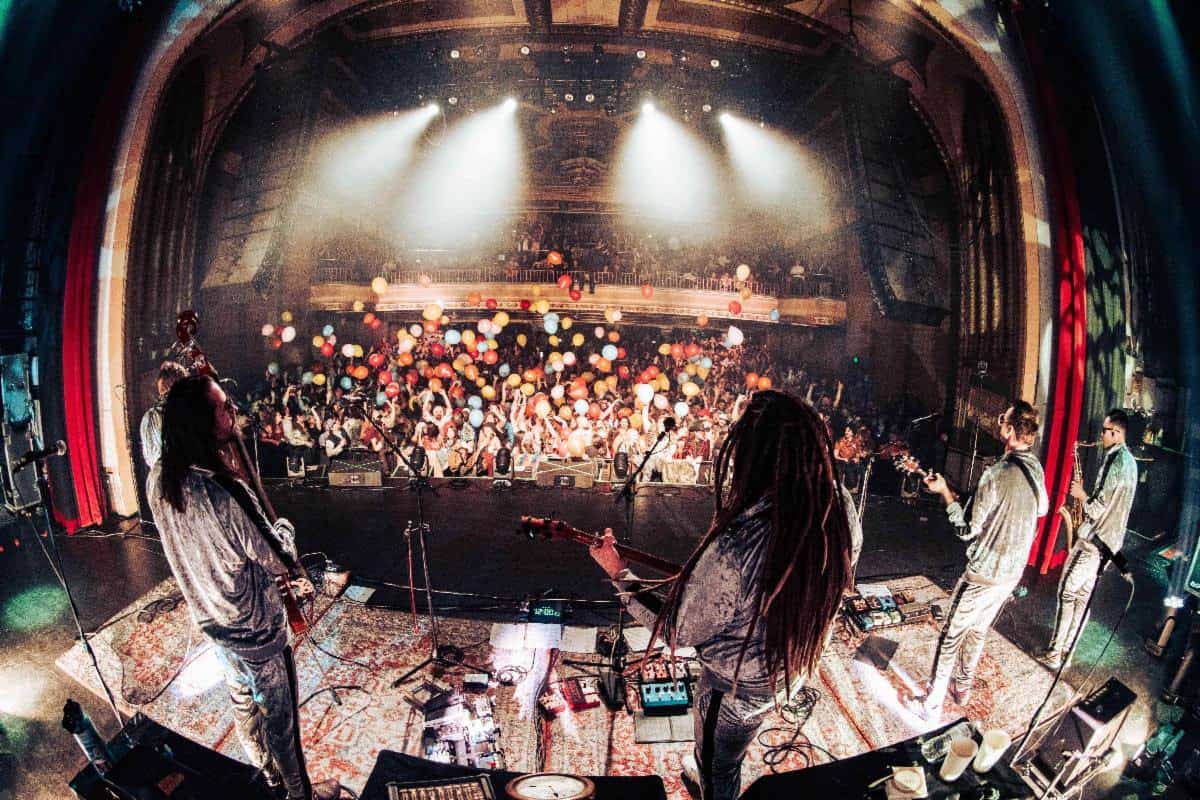 Live music concert with band performing on stage at a packed venue filled with audience and balloons, vibrant lighting, and energetic atmosphere for music industry news and event coverage.