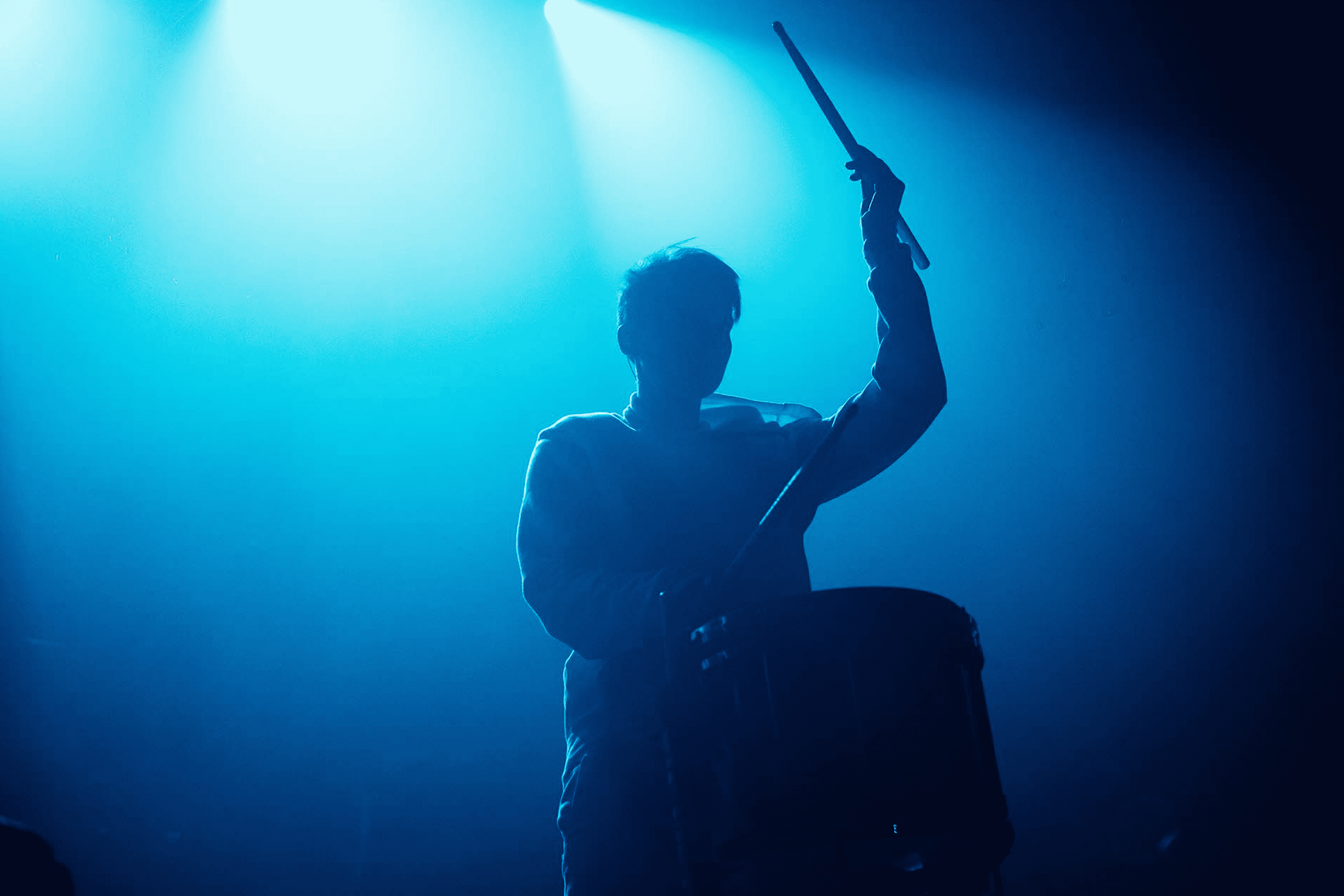 A silhouette of a musician playing drums on stage under blue lighting, creating a dramatic and energetic concert atmosphere, perfect for music industry and live performance keywords.