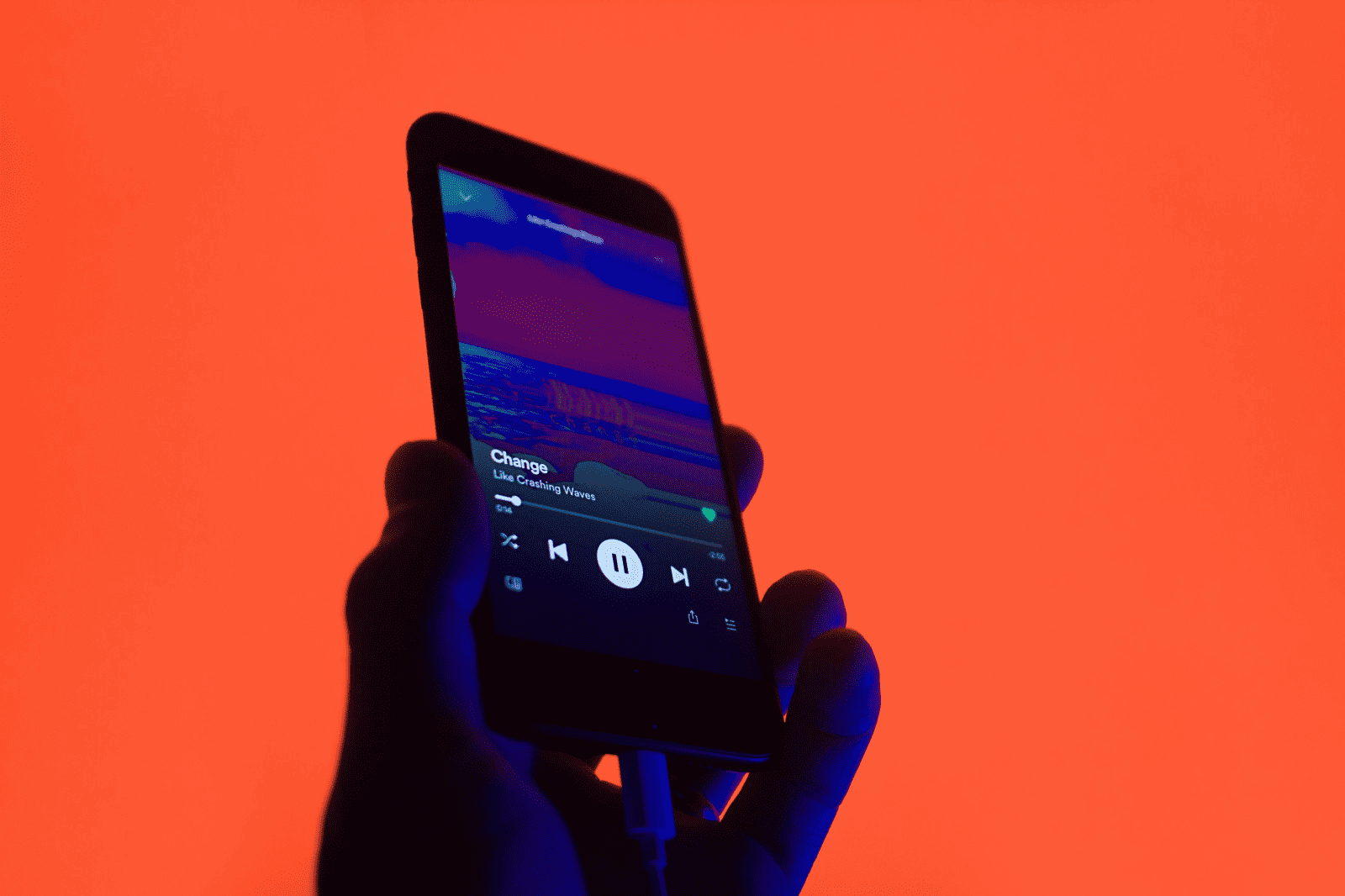 Music streaming on smartphone with ocean view album art and music controls, dark silhouette against vibrant orange background, modern digital music technology, online music listening, audio entertainment, Hypebot image relevance.