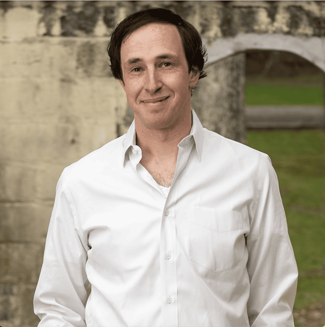Cloud-based music industry expert in white shirt smiling outdoors at historic stone building with archway.