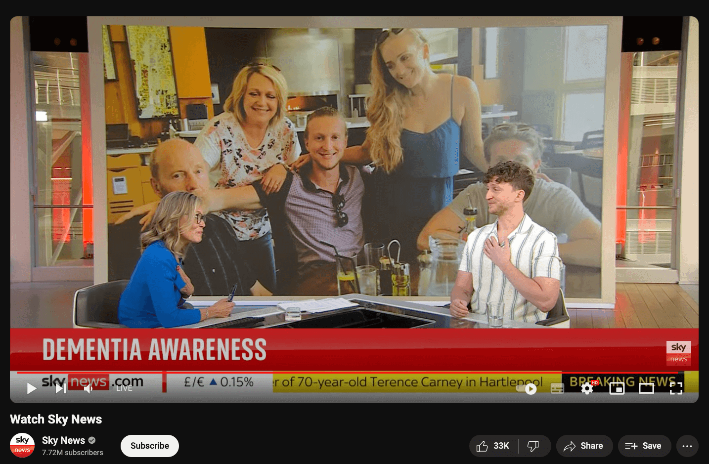 Seeing a television broadcast studio with a large screen displaying a family gathering, in a discussion about dementia awareness, with news graphics and hosts engaged in conversation.