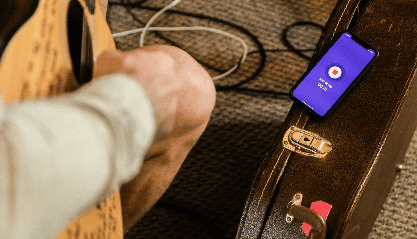 Guitar recording on phone, musician practicing with digital recorder, acoustic guitar and smartphone on guitar case, music studio setup, music production, home recording, music technology, Hypebot.