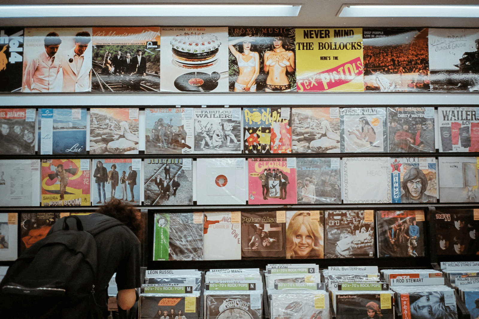 Vinyl records collection display at a music store, showcasing classic rock and pop albums, with a person browsing through vinyls, emphasizing music discovery, vinyl collection, and music lovers, in an energetic retail environment.