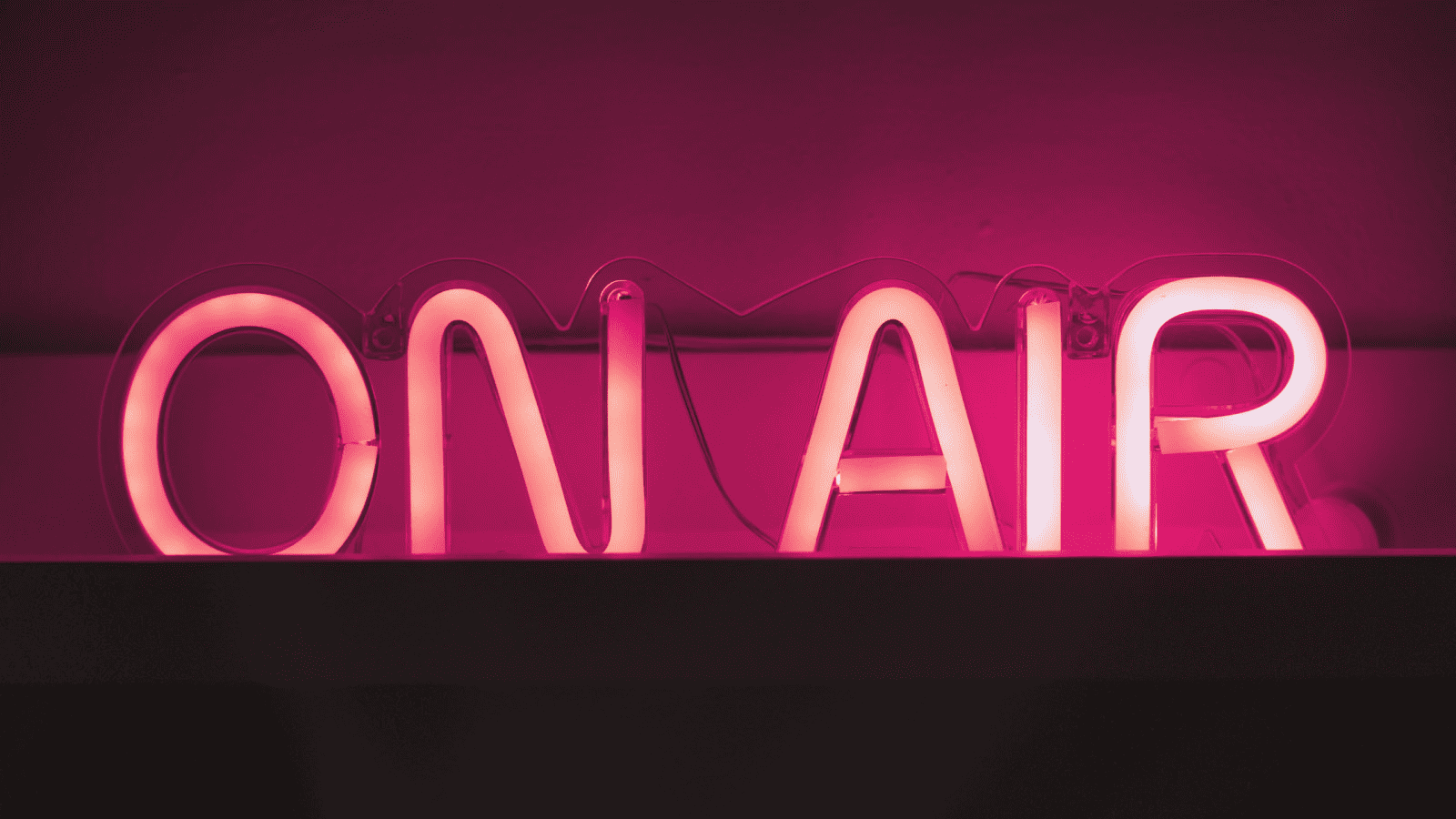 Neon "ON AIR" sign illuminated in pink, used for live broadcast or recording studio setup, vibrant indoor lighting, modern media environment, popular for podcasts and online streaming, aesthetic aesthetic.