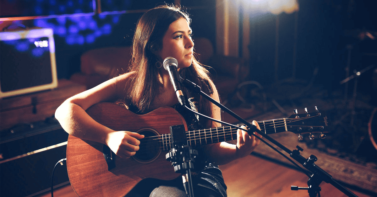 Acoustic guitar performance at a music studio, young woman singing and playing live music, musician recording in studio, music artist performing with guitar, passionate singer-songwriter in a professional setting.