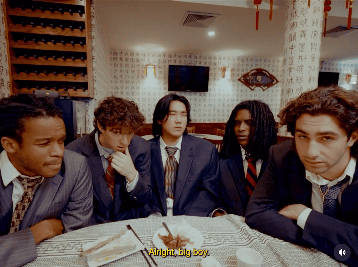 Business meeting with diverse young men in formal suits at a restaurant, discussing serious topics, urban style, casual atmosphere, diverse ethnicity, modern setting, vibrant background, social networking, team discussion, thematic of collaboration and youth culture.