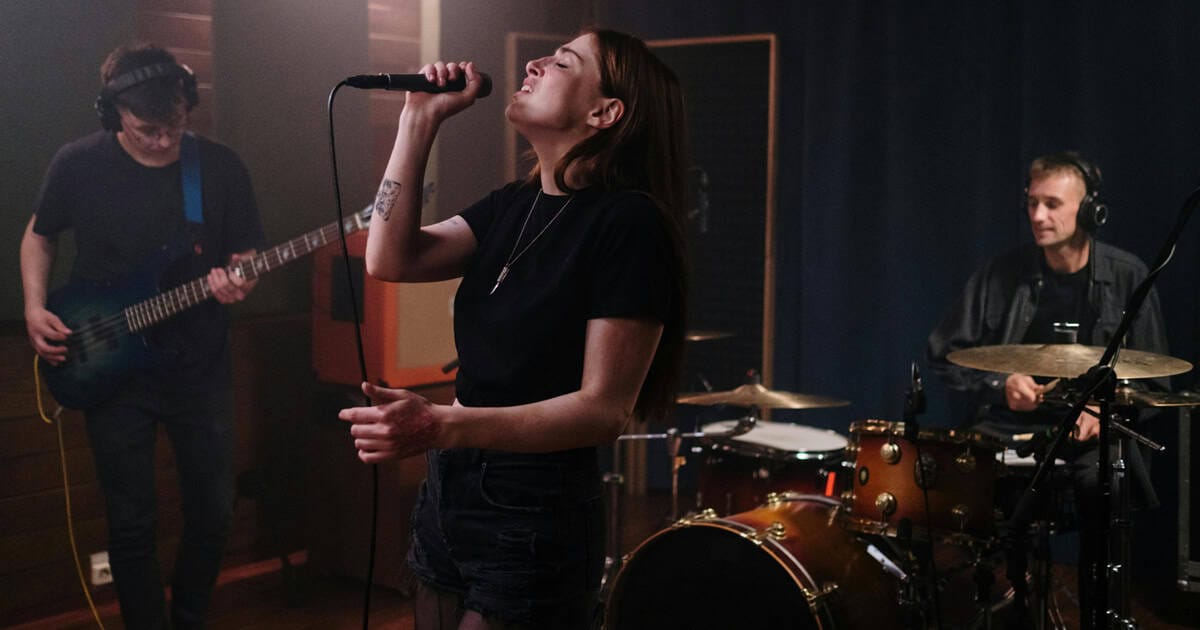 Female singer performing in recording studio with guitar and drums, showcasing live music, band practice, and music production for music industry SEO.