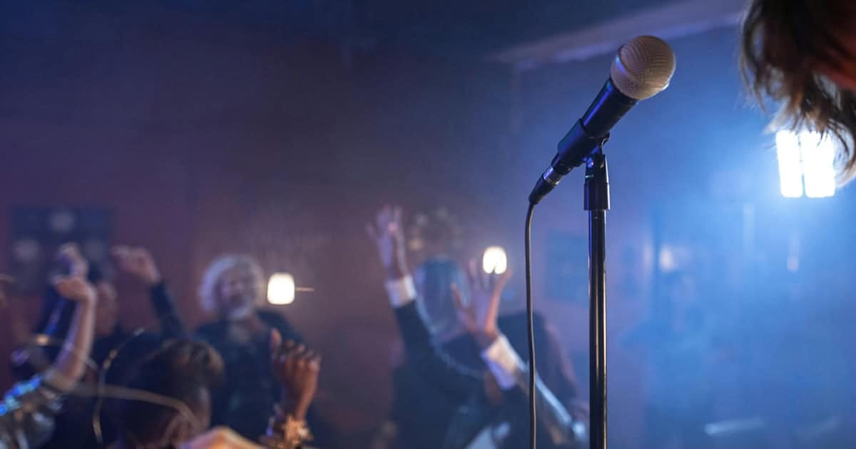 A microphone on stage with a lively audience enjoying live music and entertainment at a hype music event or concert.