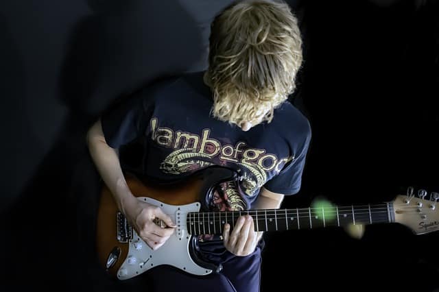 A young musician playing an electric guitar, wearing a "lambofgod" t-shirt, captured in a creative music-inspired environment.
