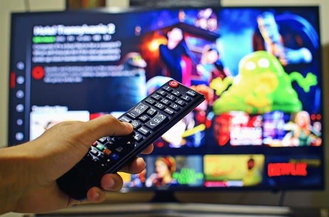 Remote control pointed at a streaming service on a smart TV screen with colorful content and Netflix logo in the background.