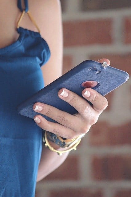 Young woman holding smartphone with jewelry and nail polish, close-up shot outdoors.