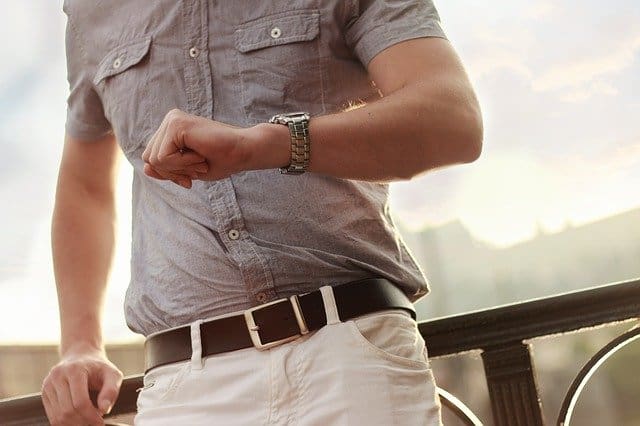 Elevated wristwatch and casual dress attire on person showing punctuality and style, standing outdoors during sunset.