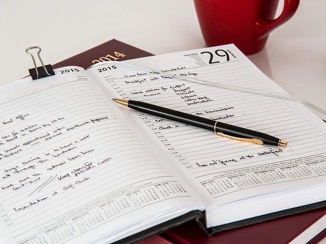 Detailed planner with handwritten notes and a pen, surrounded by a red mug and calendar, illustrating effective time management and organization.