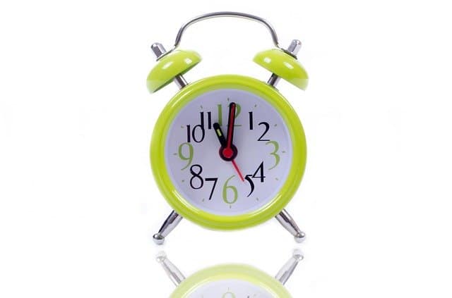 Bright green vintage alarm clock with white face and black, red, and green numbers, showing almost 12:00. Perfect for morning wake-up or time management concepts.
