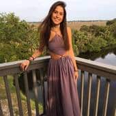 Beautiful young woman standing outdoors on a wooden bridge overlooking a river and lush green landscape, enjoying nature in a sunny setting.
