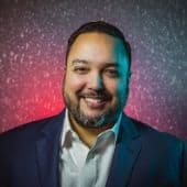 - A professional smiling man with colorful neon lights background at a music industry event.