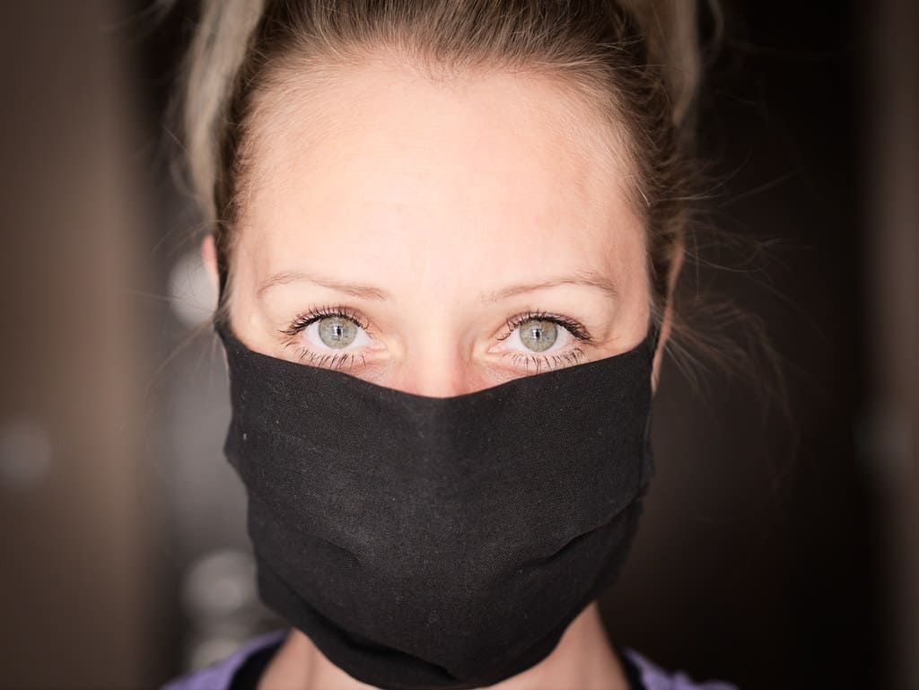 Face of a woman wearing a black face mask, close-up portrait, emphasizing eyes, safety precautions, and current health trends, with blurred background.