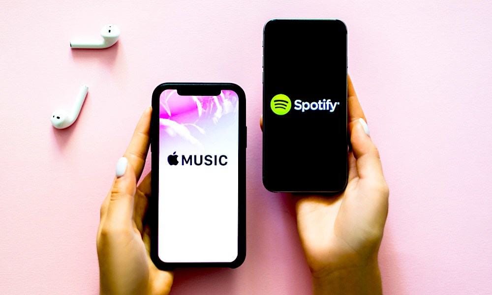 Apple Music and Spotify app screens displayed on smartphones with wireless earbuds on a pink background, highlighting popular music streaming platforms.