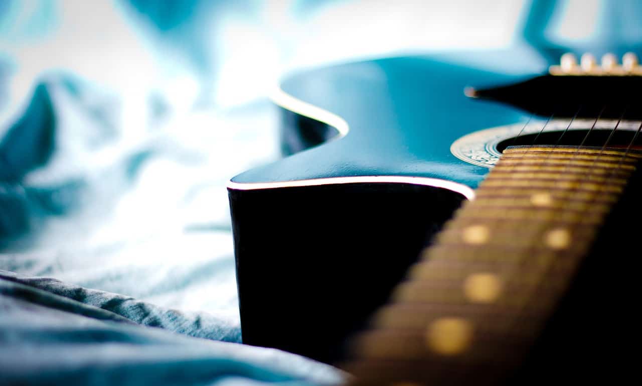 Guitar on a soft bed with natural light, showcasing musical instrument artistry.