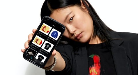 A young woman holding a smartphone displaying various music and fashion app icons, emphasizing digital music and online shopping.
