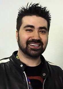 Professional man with dark hair and beard smiling in casual attire at a music industry event or conference.