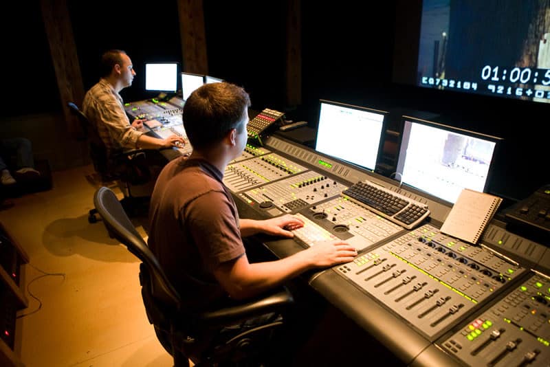 Studio sound mixing console with technicians operating modern audio equipment in a professional recording studio.