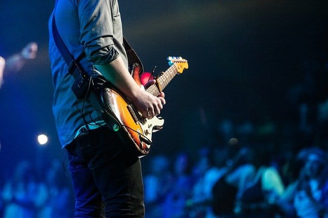 Guitarist performing live on stage with audience in the background at a concert, showcasing music performance and entertainment scenes.