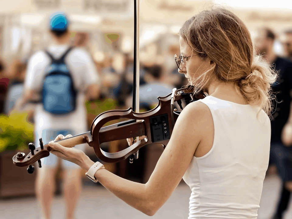 A woman playing a violin outdoors among a crowd, capturing live music performance at an event or festival, with focus on musical instrument and performer.
