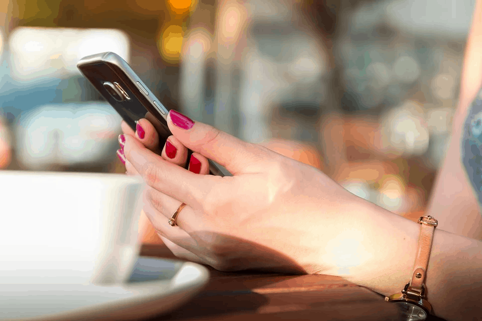 Elegant woman using smartphone with pink nail polish sitting at coffee shop for social media and digital marketing.