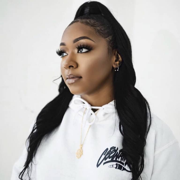 Stylish young woman with long black hair and makeup, wearing a white hoodie, looking thoughtfully to the side, showcasing modern fashion and beauty trends.