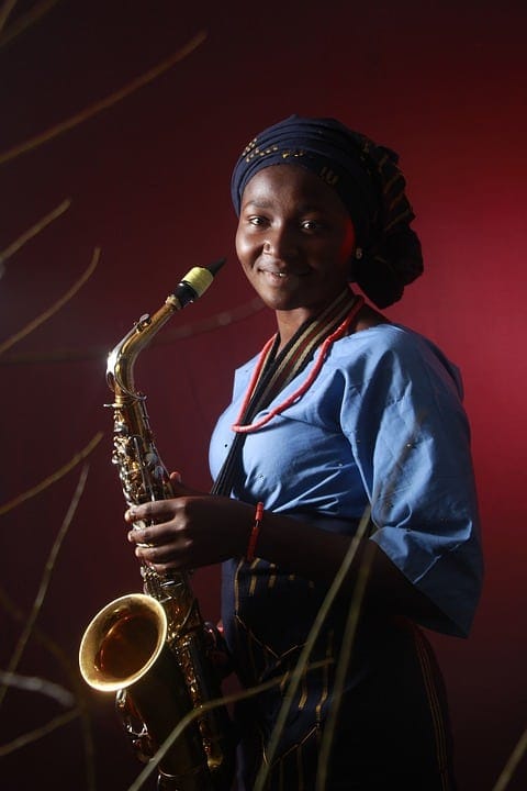 Elegant African woman holding a saxophone in traditional attire, representing cultural fusion in music, with vibrant lighting highlighting her poised expression, emphasizing jazz and world music themes.