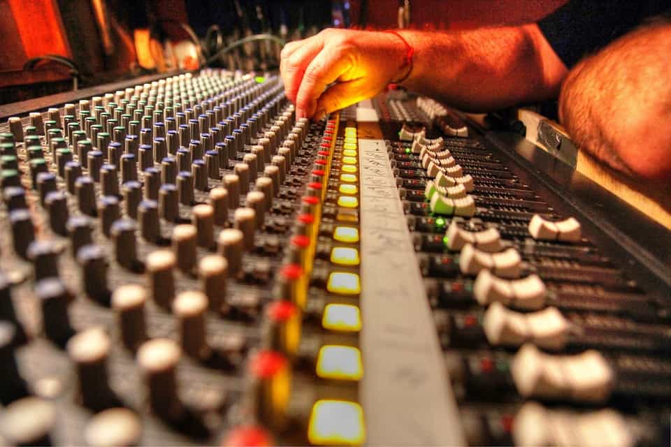 Sound engineer adjusting audio mixing console at live music venue, close-up of equipment and control knobs, professional sound mixing for concerts and events.