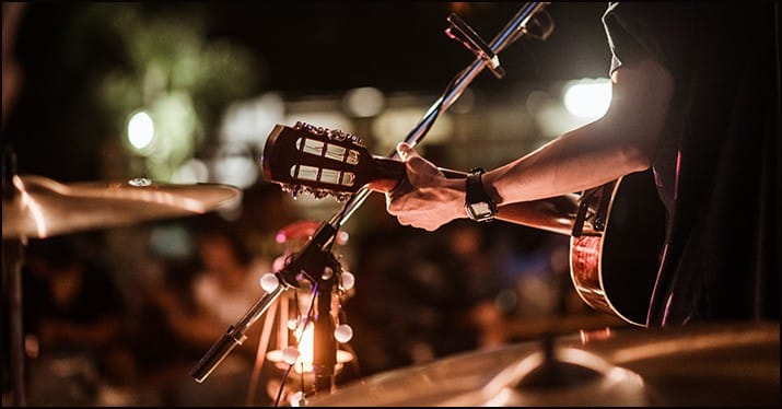 Guitarist performing live at an outdoor concert during nighttime, with audience in the background and soft stage lighting.