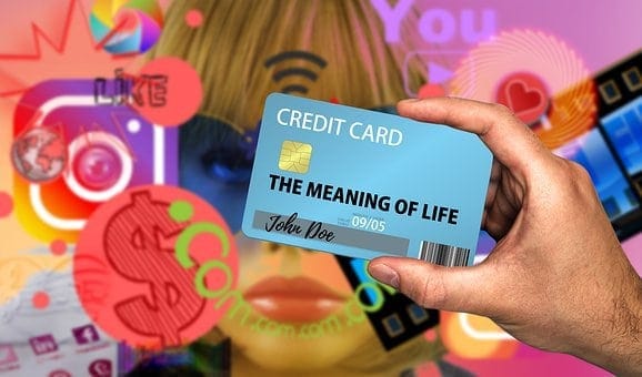 Credit card with the message "The Meaning of Life" held by a hand amid a digital background of social media icons and emojis.